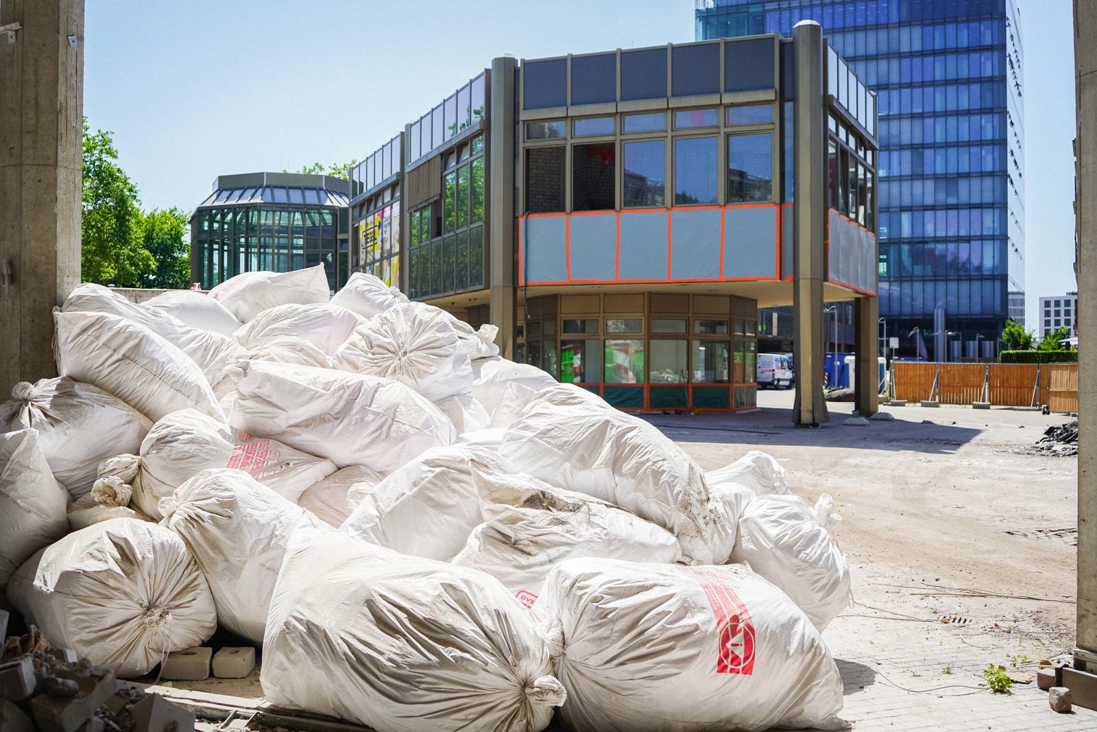 Gestapelte gefuellte Big Bags mit Bauschutt zur Entsorgung vor modernem Glasgebaeude